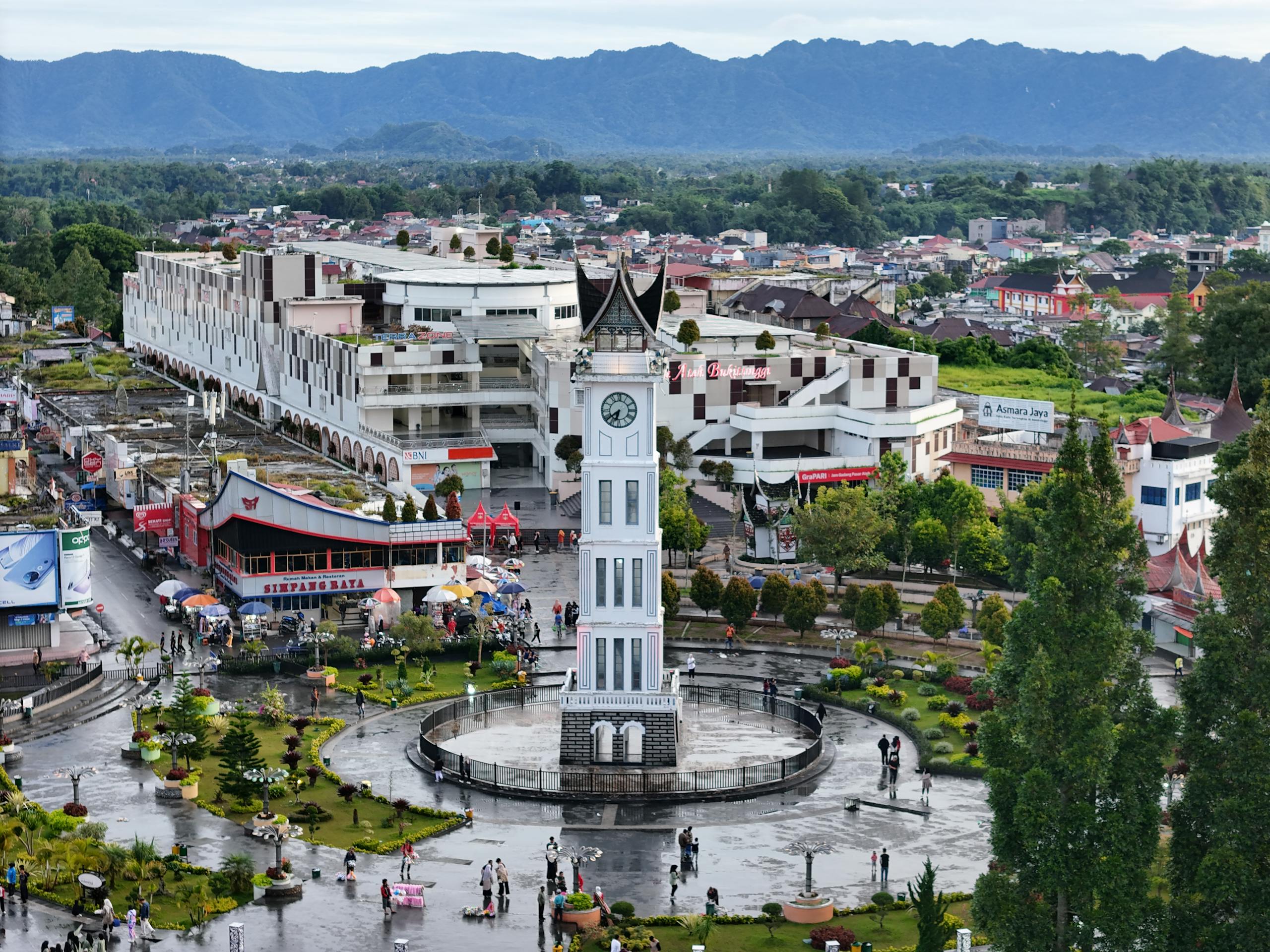 Aerial shot of Jam Gadang tower in Bukittinggi, Indonesia, showcasing the vibrant town square and mountainous backdrop.